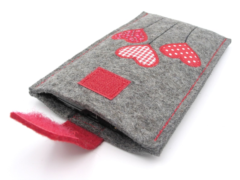 May include: A grey felt phone case with a red felt flap and three red felt hearts with white polka dots and gingham patterns.