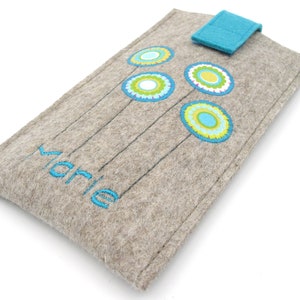 May include: A gray felt phone case with a blue flap closure. The case has a blue and green floral design and the name "Marie" embroidered on the front.