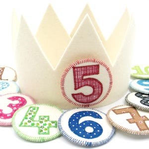 May include: A white felt crown with a red felt number 5 on the front. There are nine felt circles with numbers 1 through 10 around the crown.