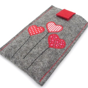 May include: Grey felt phone case with a red felt flap closure. Three red felt hearts with different patterns are stitched on the front of the case.