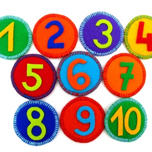 Könnte beinhalten: Zehn bunte Filz-Kreise mit den Zahlen 1 bis 10, die darauf gestickt sind. Die Kreise sind in einer Halbkreisform angeordnet.