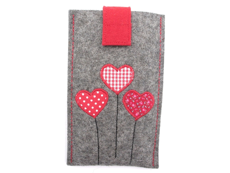May include: Grey felt phone case with three red felt hearts. The hearts are decorated with white polka dots, red and white gingham, and a pink floral pattern.