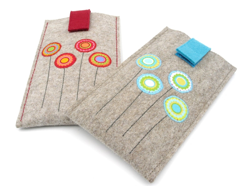 May include: Two gray felt phone cases with colorful embroidered flowers. One case has red flowers and a red flap closure. The other case has blue flowers and a blue flap closure.