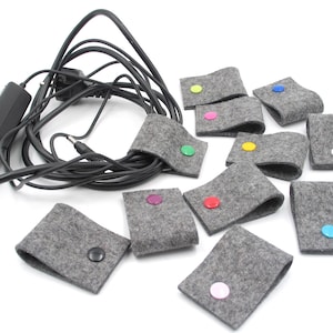 Può includere: Un set di dieci organizzatori per cavi in feltro grigio con bottoni colorati. Gli organizzatori sono progettati per mantenere i cavi e i fili in ordine e organizzati.