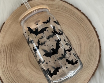 May include: A clear glass tumbler with a bamboo lid and a clear straw. The tumbler is decorated with a pattern of black bats. The tumbler is sitting on a round wooden slice.