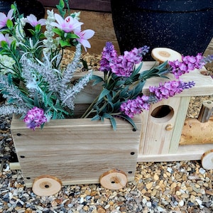 May include: A wooden train planter filled with purple and pink flowers. The train has wooden wheels and a natural wood finish. The flowers add colour to the rustic design, ideal for garden decor.