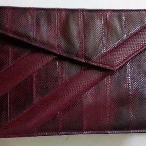 May include: A burgundy snakeskin clutch purse with a flap closure and a long strap.