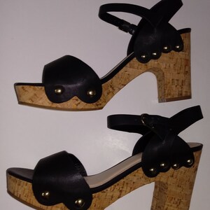 May include: A pair of black cork wedge sandals with ankle straps and gold accents. The sandals have a cork platform and a cork heel.