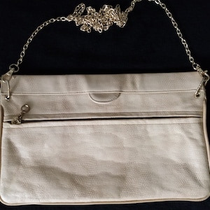 May include: A light beige leather clutch purse with a gold chain strap. The purse has a flap closure and a zippered pocket on the front.