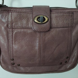 May include: A mauve leather crossbody bag with a flap closure and a metal buckle. The bag has a small pocket on the front and decorative studs around the bottom.