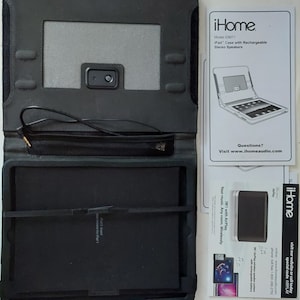 May include: Black iPad case with built-in speakers. The case has a flap that folds over the screen and a headphone jack on the side. The case is open and the iPad is not visible. The case is next to a white instruction manual with the text "iHome Model IDM71 iPad Case with Rechargeable Stereo Speakers" and "Questions? Visit www.ihomeaudio.com".
