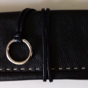 May include: A black leather clutch with a white stitch detail and a silver ring closure.