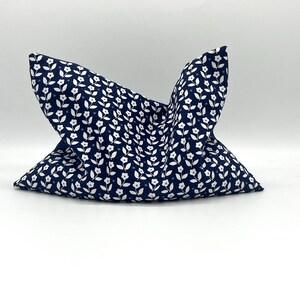 Könnte beinhalten: Ein marineblaues Kissen mit einem weißen Blumenmuster. Das Kissen ist in einer einzigartigen Form gefaltet, wodurch das Design des Stoffes hervorgehoben wird. Das Blumenmuster besteht aus kleinen weißen Blüten und Blättern und erzeugt eine zarte und charmante Ästhetik. Das Kissen ist wahrscheinlich für die Inneneinrichtung.