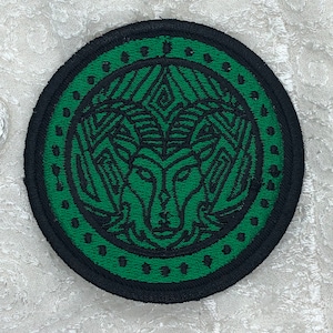 Op de afbeelding: Een groene en zwarte geborduurde patch met een gestileerd wolfskopontwerp. De wolfskop is omgeven door een zwarte cirkel met een groene buitenring.
