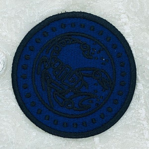 May include: A dark blue embroidered patch with a black scorpion design inside a circle. The circle is outlined with a black border and has a repeating pattern of small black dots.
