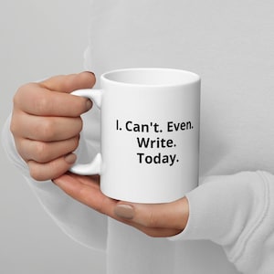 May include: A white ceramic mug with the text "I. Can't. Even. Write. Today." printed in black. The mug has a curved handle and is held by a person.
