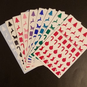 May include: A set of ten sheets of Christmas-themed stickers. Each sheet features a different color and design, including red, green, blue, purple, and black. The stickers feature various Christmas icons, such as trees, presents, candy canes, and Santa Claus.