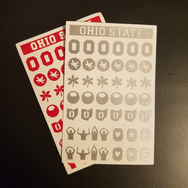 May include: Two sheets of stickers featuring Ohio State University logos and symbols. The stickers are white with gray designs. The top sheet features the words "Ohio State" in white letters. The bottom sheet features the words "Ohio State" in red letters.