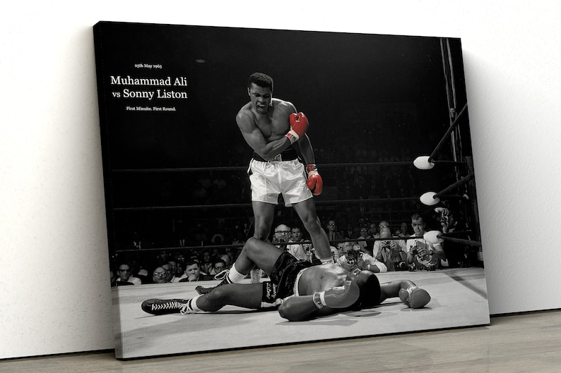 May include: Black and white photo of a boxing match between Muhammad Ali and Sonny Liston. The photo shows Ali standing over Liston, who is lying on the ground. The text "25th May 1965, Muhammad Ali vs Sonny Liston, First Minute, First Round" is visible in the top left corner of the photo.
