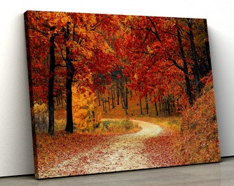 May include: A canvas print of an autumn forest scene. The image features a winding dirt path through a forest with trees displaying vibrant red and orange foliage. Fallen leaves cover the path.