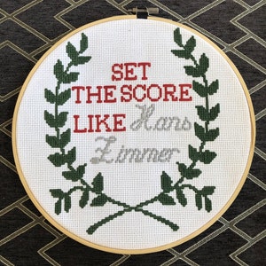 Puede incluir: Aro de bordado blanco con un diseño de corona verde y el texto "Set the score like Lamar Jackson".