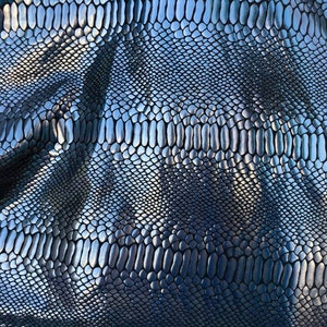 Puede incluir: Primer plano de una tela de piel de serpiente plateada con un patr&oacute;n texturizado y escamoso.