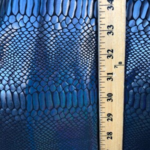 Puede incluir: Primer plano de una tela de piel de serpiente azul y negra iridiscente con una regla que mide 89 cm.