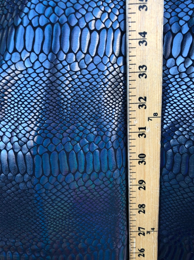Puede incluir: Primer plano de una tela de piel de serpiente azul y negra iridiscente con una regla que mide 89 cm.