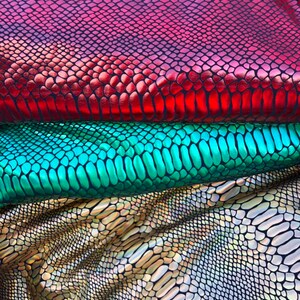 Puede incluir: Tres piezas de tela iridiscente con un patr&oacute;n de piel de serpiente. La pieza superior es roja, la pieza del medio es verde y la pieza inferior es dorada.