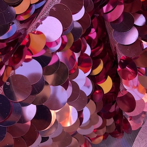 May include: Pink, gold, and red iridescent sequins on a sheer mesh fabric. The sequins are arranged in a scale-like pattern.