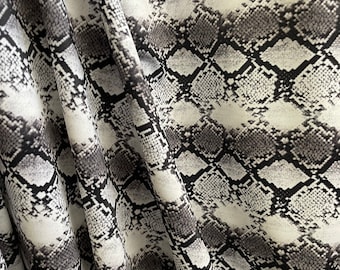 May include: Close-up of a white fabric with a black snake skin pattern. The fabric is wrinkled and has a soft texture.