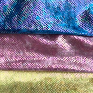 May include: Three swatches of iridescent fabric with a scale pattern. The top swatch is blue, the middle swatch is purple, and the bottom swatch is green.