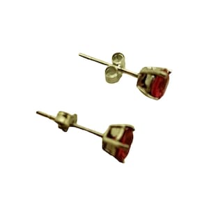 May include: A pair of silver stud earrings with a red gemstone in each. The earrings have a simple design and are perfect for everyday wear.