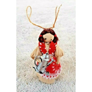Peut inclure: Ornement de poupée fait à la main en écorces de maïs, vêtue d'une robe rouge à pois blancs et d'une écharpe assortie. La poupée tient une petite théière argentée. L'ornement a des cheveux bruns et une ficelle pour l'accrocher.