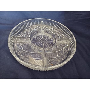 Puede incluir: Un plato de servir de vidrio transparente con cuatro secciones y un hueco central. El plato tiene un patrón decorativo de vidrio cortado.