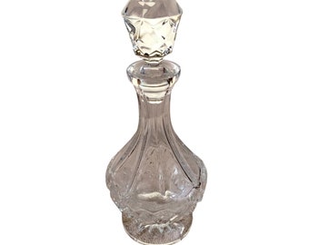 May include: A clear glass decanter with a faceted stopper. The decanter has a round body with a textured surface.