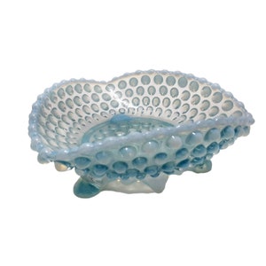 Puede incluir: Un tazón de vidrio azul claro con una superficie texturizada y con burbujas. El tazón tiene un borde festoneado y se asienta sobre tres pequeños pies.