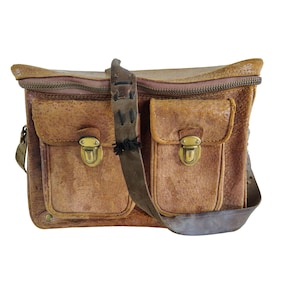 Puede incluir: Bolso de cuero marrón con dos bolsillos delanteros, cada uno asegurado con un cierre de color latón. El bolso tiene una correa larga y ajustable para el hombro y un cierre de cremallera en la parte superior. El cuero tiene un aspecto envejecido.