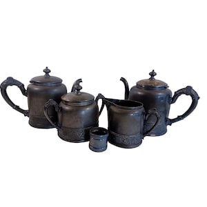 May include: A silver tea set with a teapot, creamer, sugar bowl, and a lidded cup. The set has a dark, aged finish and intricate floral designs.
