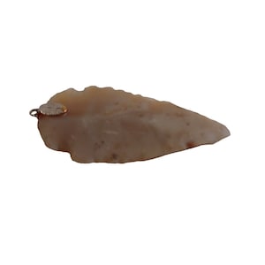 以下が含まれることがあります： 銀色の金属製のループが付いた薄い茶色の矢じりペンダント。矢じりは、不規則でざらざらした形をした天然石です。