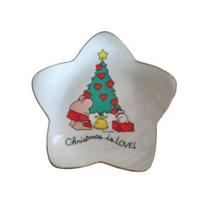 May include: Star-shaped ceramic dish with a gold rim. The dish features a Christmas tree decorated with heart-shaped ornaments, a hippo, a dog, and the text "Christmas is LOVE!"
