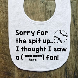May include: White baby bib with a baseball graphic and the text "Sorry for the spit up... I thought I saw a (team name) fan!"