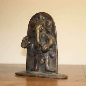 May include: A bronze statue of the Hindu deity Ganesha, the elephant-headed god of wisdom and prosperity. The statue is standing on a rectangular base and is depicted with his trunk curled up to his mouth, holding a sweetmeat in his lower right hand, and a small axe in his upper left hand.