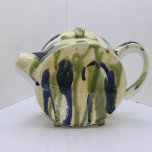 Könnte beinhalten: Eine weiße Teekanne aus Keramik mit rundem Korpus und Henkel. Die Teekanne ist mit grünen und blauen abstrakten Mustern verziert.
