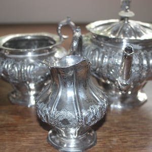 May include: A silver tea set with intricate floral designs. The set includes a teapot, creamer, and sugar bowl.
