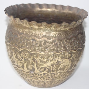 Pode incluir: Pote de metal antigo cor de latão com borda ondulada. O pote apresenta entalhes em relevo detalhados de árvores, animais e padrões florais. O pote tem formato arredondado e provavelmente é usado para fins decorativos.