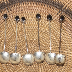 Puede incluir: Juego de seis cucharaditas de plata con mangos de piedra preciosa negra. Las cucharas tienen un diseño floral y están dispuestas sobre una superficie tejida.