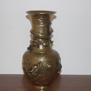 Pode incluir: Um vaso grande, ornamentado, de cor dourada com talhas e desenhos intrincados. O vaso tem uma boca larga e um corpo redondo.