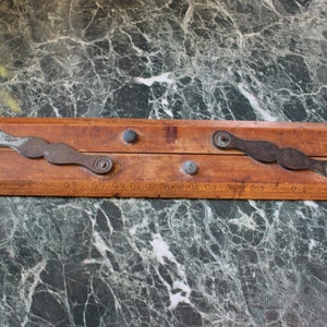 May include: A wooden folding ruler with metal hinges and a scale marked in inches. The ruler is closed and has two metal rivets on each side.
