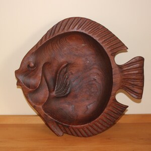 May include: A dark brown wooden fish-shaped serving dish. The dish is carved with details and has a slightly rounded shape.